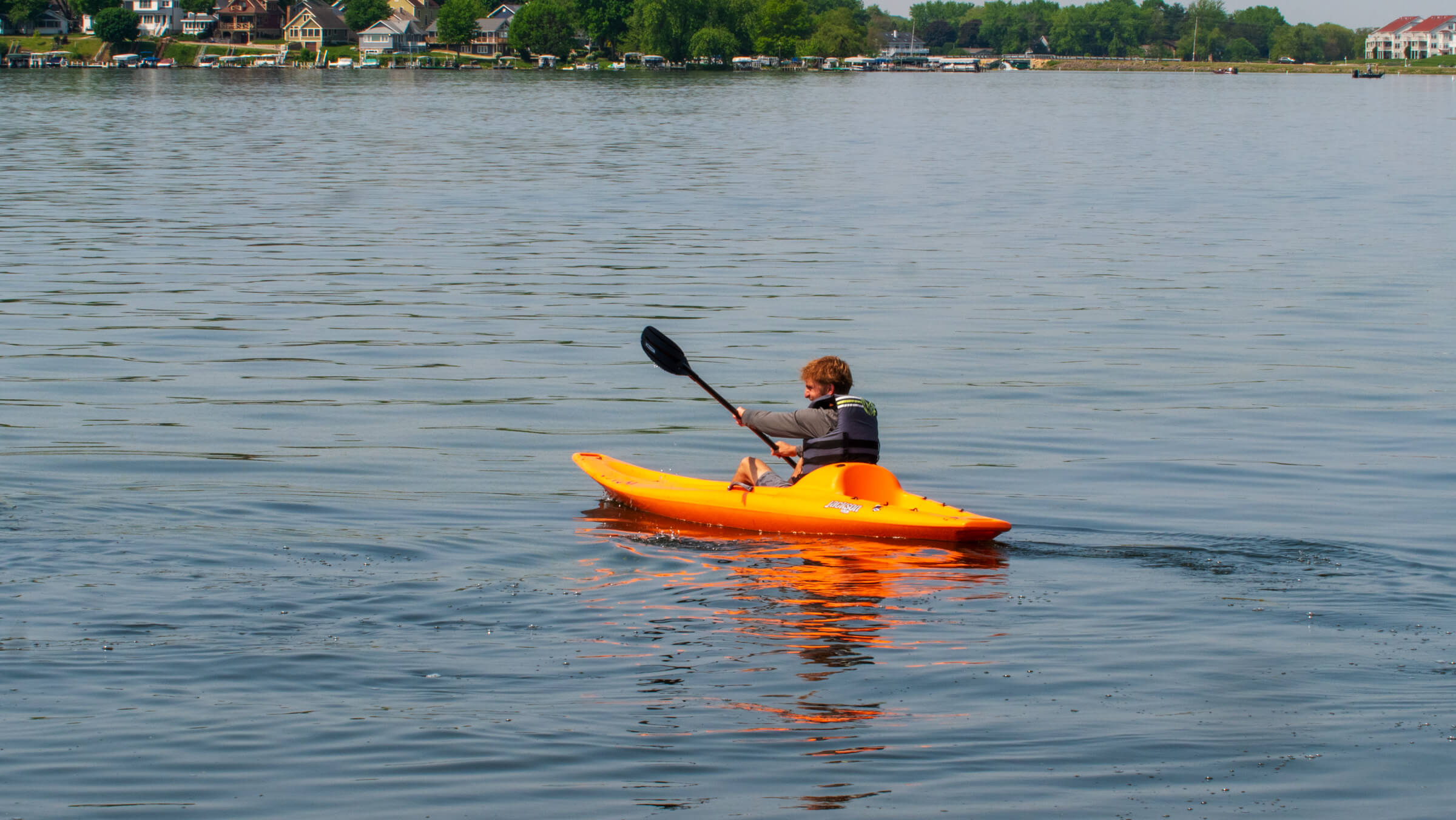 A young man kayaking on Delavan Lake. The kayak is orange, and the lake is calm.