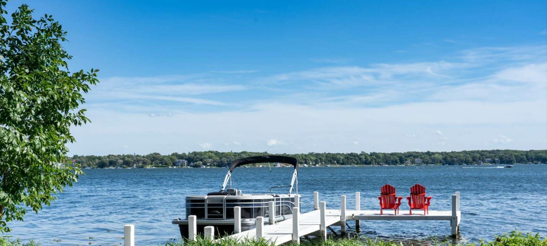 Pier at Lake Lawn Resort. The pier is white, has a pontoon docked at it, and has two red chairs sitting at the end.