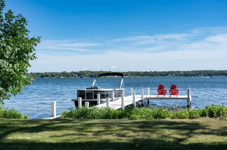 Pier at Lake Lawn Resort. The pier is white, has a pontoon docked at it, and has two red chairs sitting at the end.