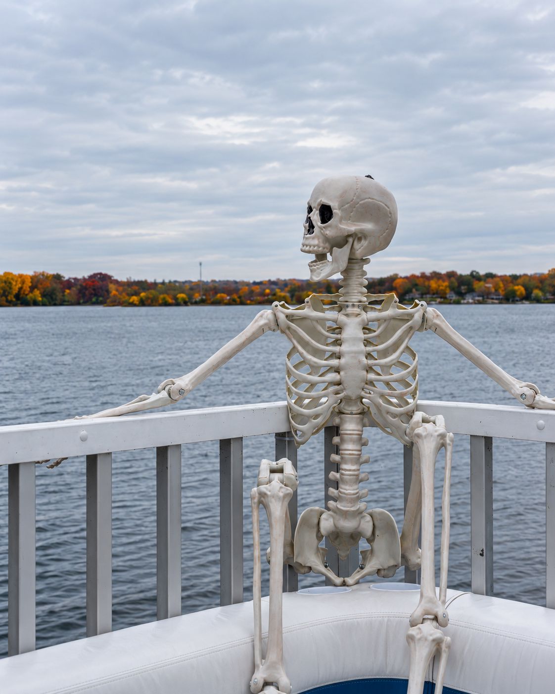 Skeleton at the rail of the Lake Lawn Queen with fall colors across Delavan Lake